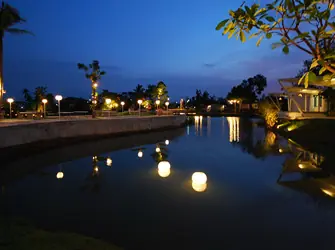 สระน้ำกลางร้านยามค่ำ มีโคมลอยน้ำและเสาไฟเรียงตามทางเดินริมน้ำ
